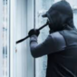 masked robber attempting to break into a commercial building at night, using tools to force open a locked door under dim security lighting.