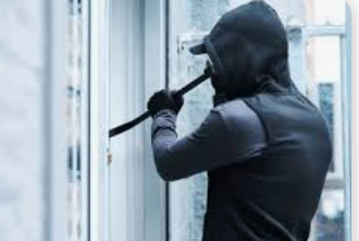 masked robber attempting to break into a commercial building at night, using tools to force open a locked door under dim security lighting.