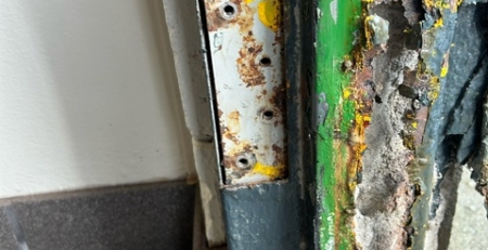 Frame section with peeling paint, rust, and concrete deterioration