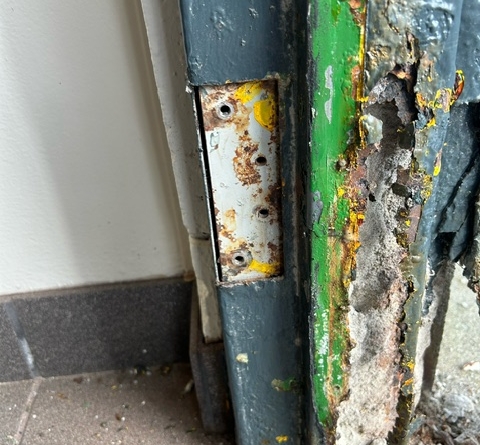 Frame section with peeling paint, rust, and concrete deterioration