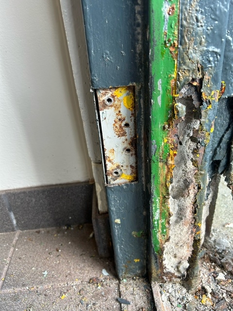 Frame section with peeling paint, rust, and concrete deterioration
