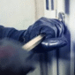 Gloved hand using a crowbar to force open a commercial door lock