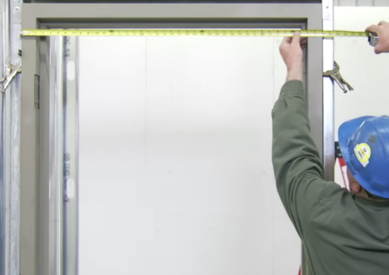 Technician measuring a hollow metal door frame during commercial door installation in Vancouver.