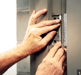 Technician installing a commercial door hinge on a steel door frame in Vancouver.