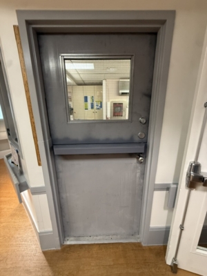 Gray commercial steel Dutch door with a vision panel in the upper section, viewed from a service area.