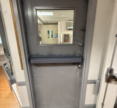 Gray commercial steel Dutch door with a vision panel in the upper section, viewed from a service area.