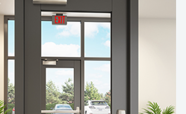 Commercial glass entrance door with overhead door closer and panic exit bar.
